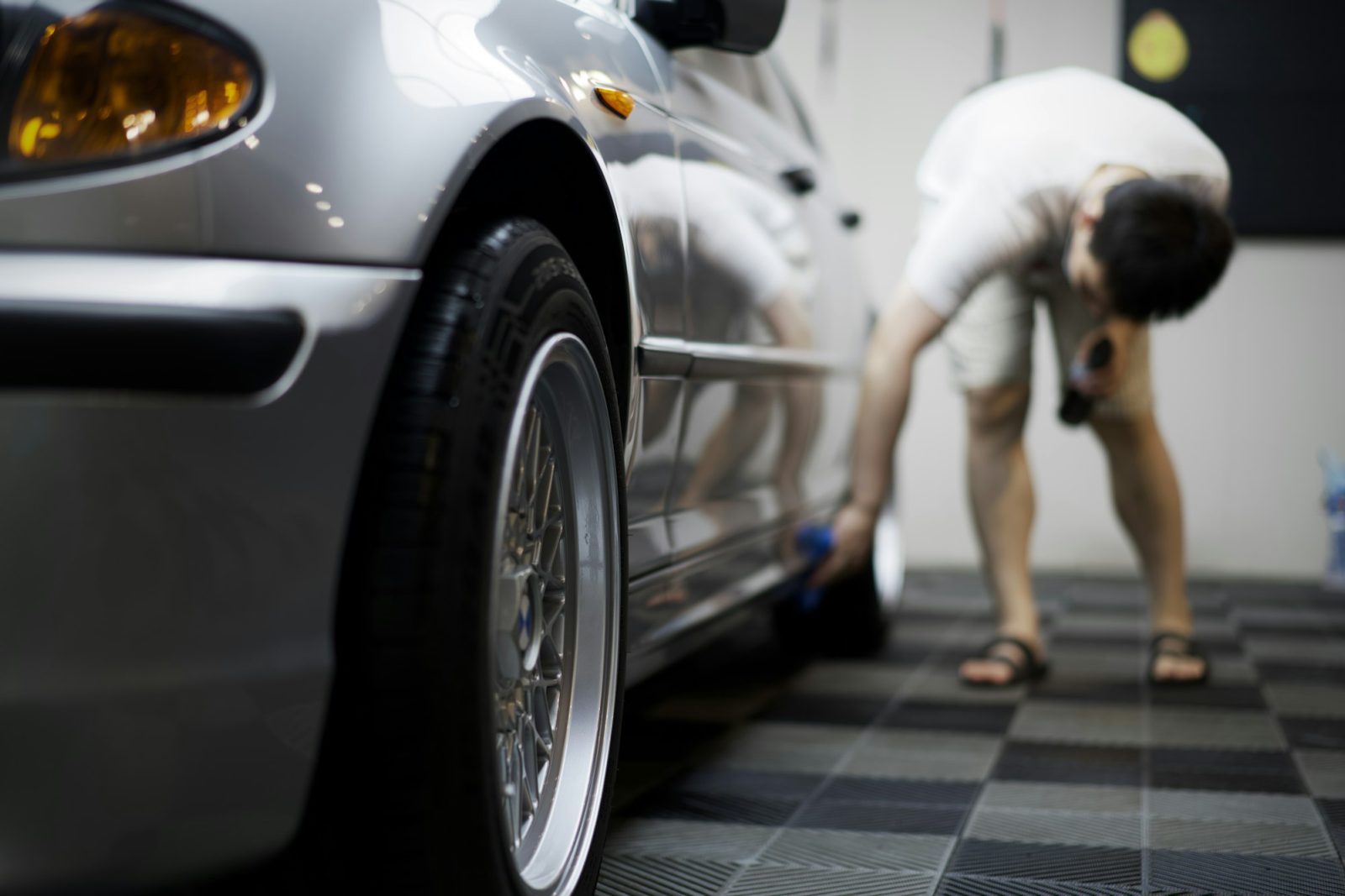 Man cleaning the wheel of a silver car in a garage
