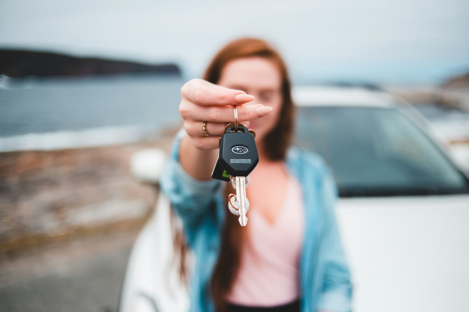 Woman holding up car keys in front of a white car