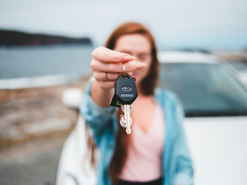 Woman holding up car keys in front of a white car