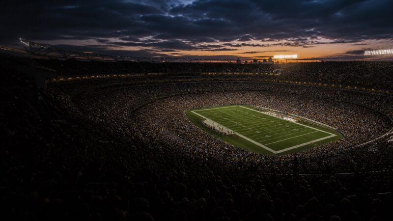 A packed stadium bowl at dusk as the floodlights come up.