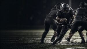 A running back hits a crease between blockers, spraying turf.