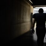 A lone player walks a dark tunnel towards the stadium light.