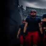 Visiting players in navy and red walk out into a loud home stadium.
