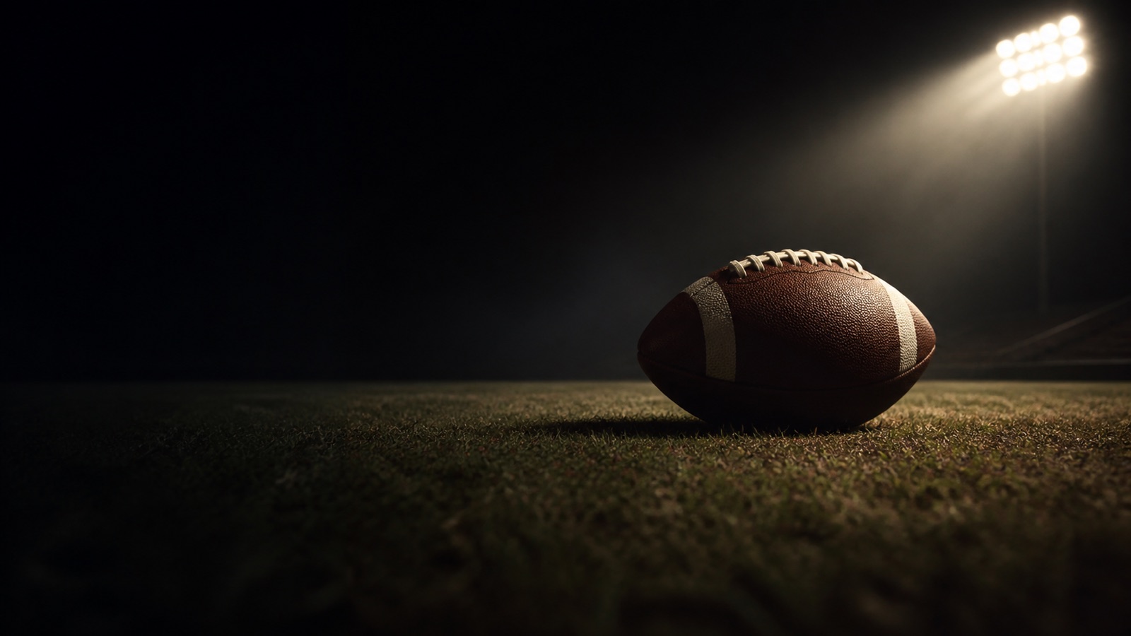A single football rests on an empty floodlit field.
