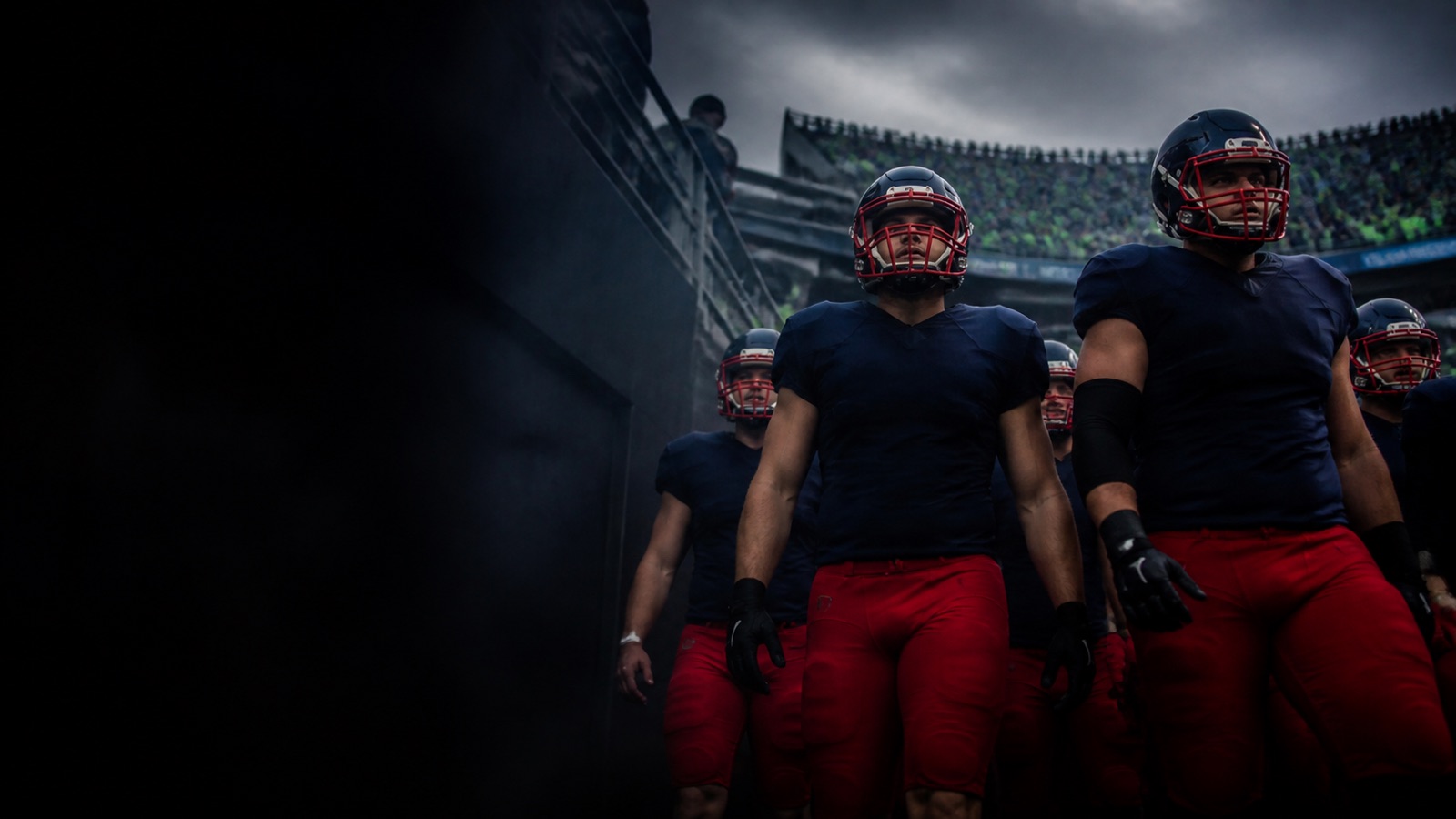 Visiting players in navy and red walk out into a loud home stadium.