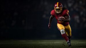 A running back in scarlet and gold cuts upfield with a taped knee.