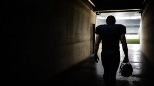 A lone player walks a dark tunnel towards the stadium light.