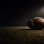 A single football rests on an empty floodlit field.