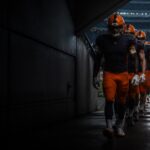 Visiting players in navy and orange take the field against the home side.